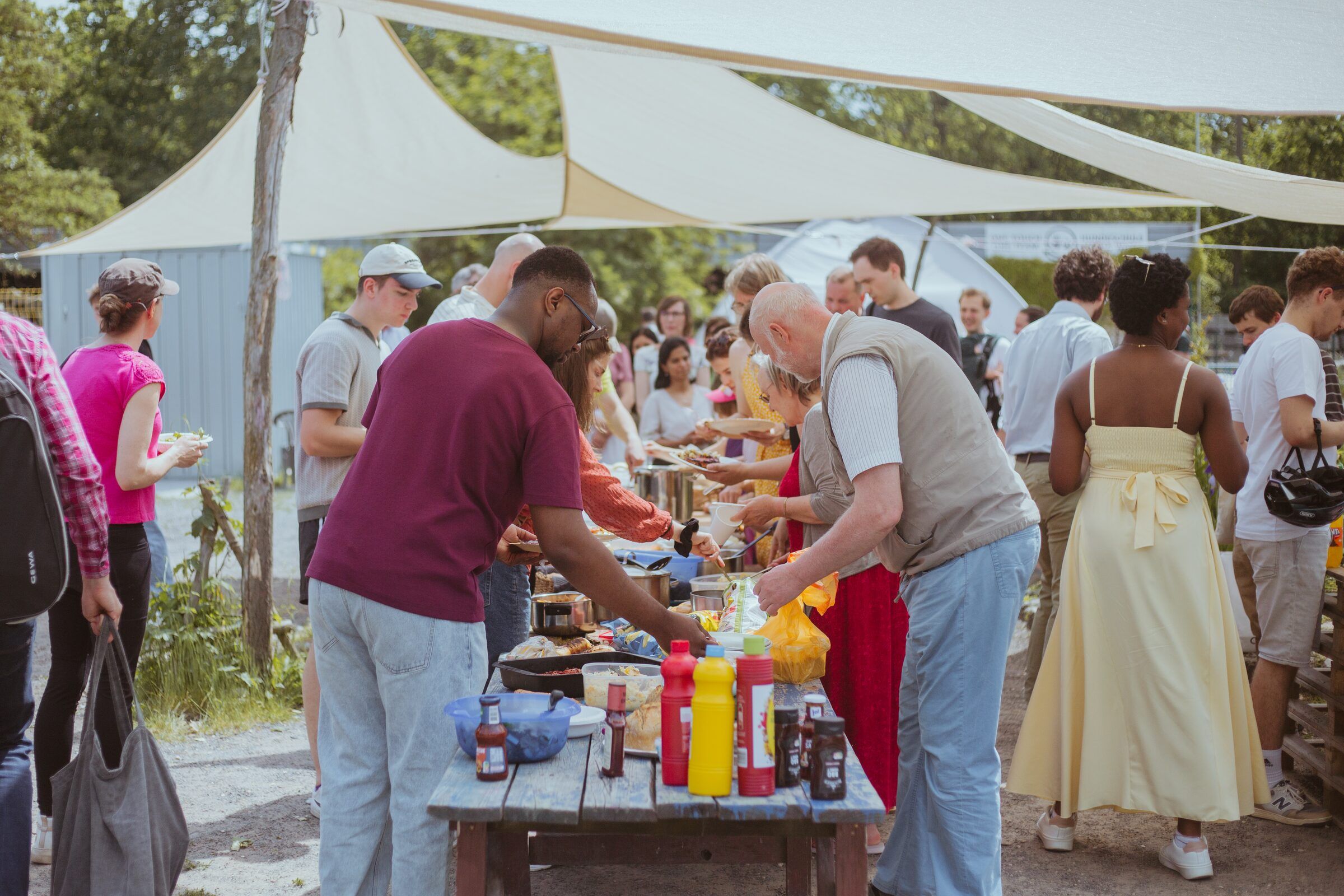 Menschen grillen und essen gemeinsam draußen unter Sonnensegeln